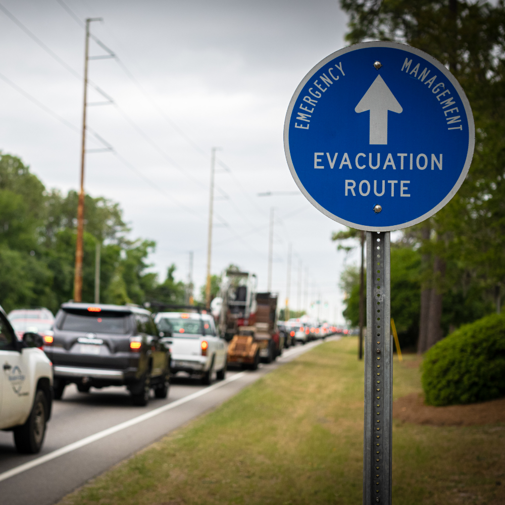 Emergency management evacuation route sign beside a line of vehicles.