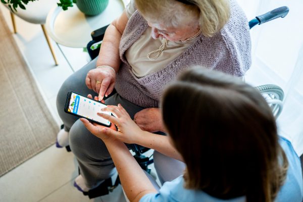 Senior woman learning to order food online with caregiver assistance, using smartphone.
