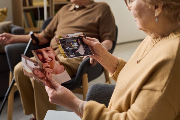 Senior woman holding family photos and discussing memories during support session, representing aging, reminiscence, dementia care. Useful for healthcare, senior living, caregiving campaigns